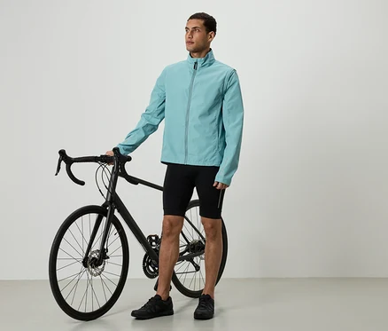 Un homme en veste bleu clair et short noir se tient à côté d'un vélo noir.