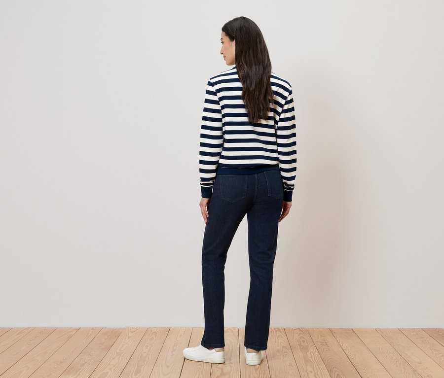 Vue de dos d'une femme aux longs cheveux foncés portant un pull rayé, un jean et des chaussures blanches.