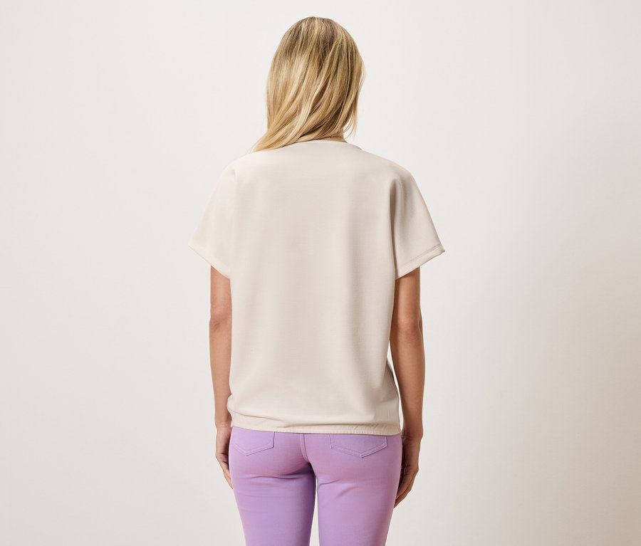 Vue arrière d'une femme aux cheveux blonds portant un haut beige et un pantalon violet.