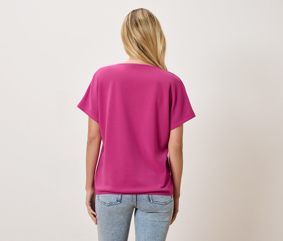 Vue de dos d'une femme blonde portant un t-shirt rose et un jean bleu clair.