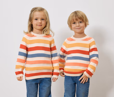 Deux enfants se tiennent côte à côte, portant des pulls rayés et des jeans.