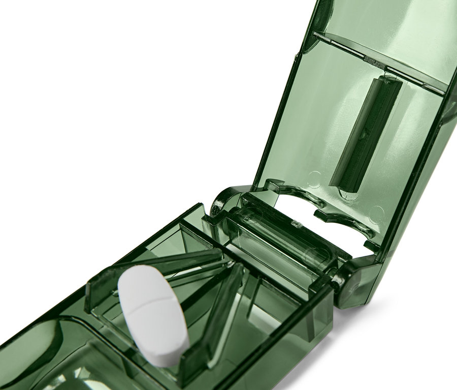 Un comprimé blanc repose dans un diviseur de comprimés vert ouvert.