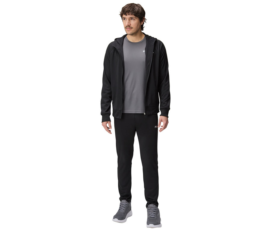 Homme portant un survêtement noir à capuche, un t-shirt gris, un pantalon de survêtement noir et des baskets grises.
