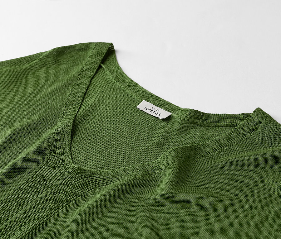 Gros plan sur un t-shirt vert à col en V avec une étiquette indiquant « TCHIBO MY STYLE ».