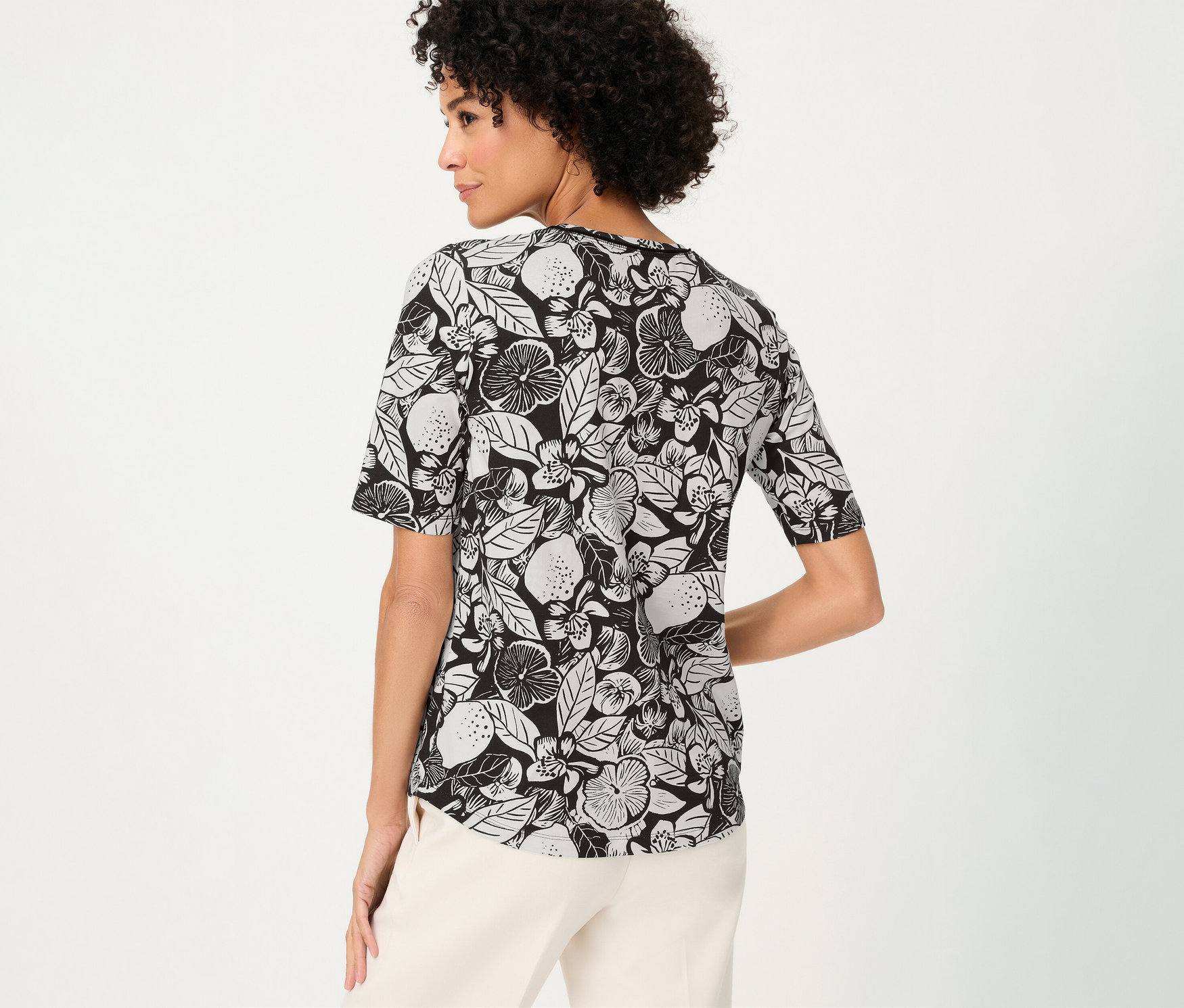 Femme de dos portant un T-shirt Olsen à motifs noirs et blancs et un pantalon clair.