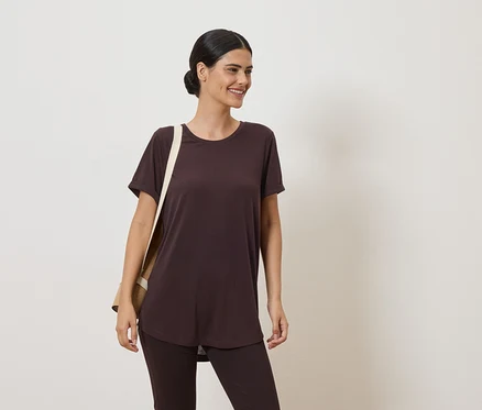 Une femme portant un chignon porte un t-shirt et un legging marron. Un sac en toile beige est sur son épaule.