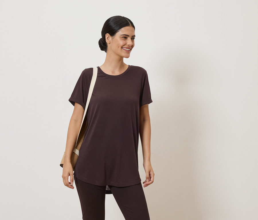 Une femme portant un chignon porte un t-shirt et un legging marron. Un sac en toile beige est sur son épaule.