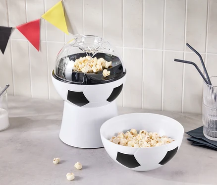 Une machine à pop-corn en forme de ballon de football se trouve à côté d'un bol de pop-corn et d'un verre avec des pailles.
