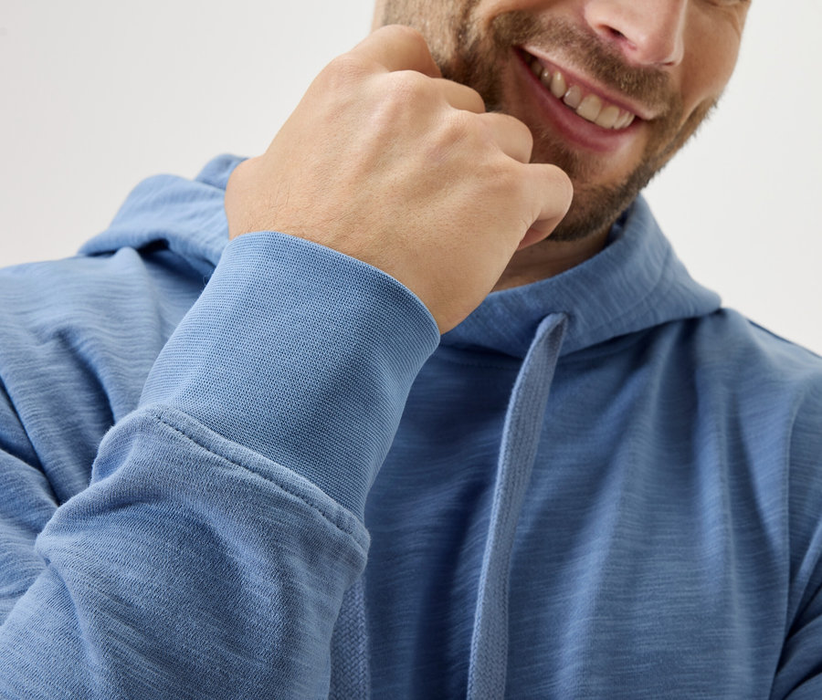 Homme souriant avec un sweat à capuche bleu touchant son menton.