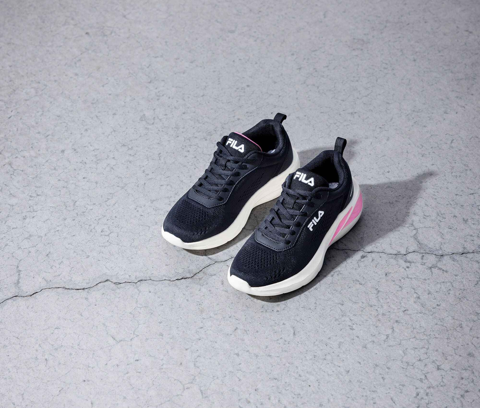 Deux baskets Fila noires posées sur un sol en béton gris.