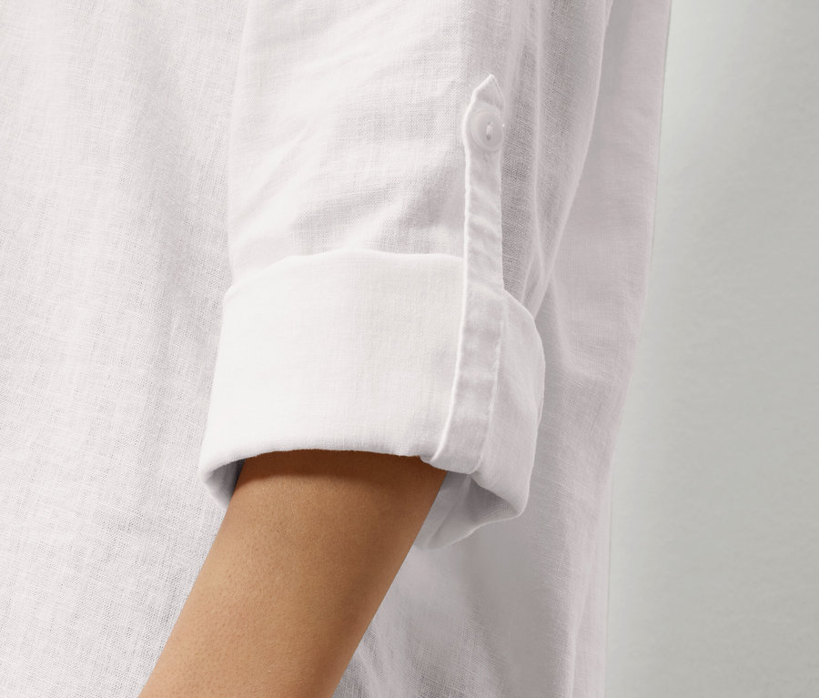 Gros plan sur la manche d'une chemise en lin blanche avec une manche retroussée et un bouton.