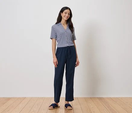 Une femme se tient devant un mur, portant une chemise géométrique bleue et un pantalon bleu marine.