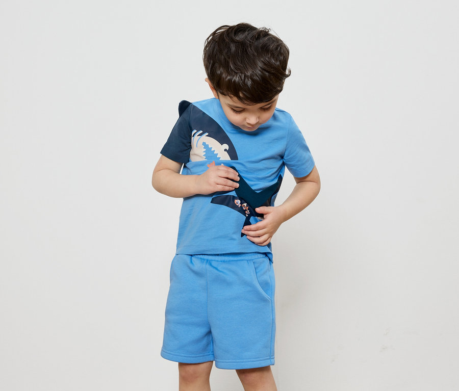 Un garçon regarde un t-shirt bleu avec un appliqué de requin, assorti à un short.