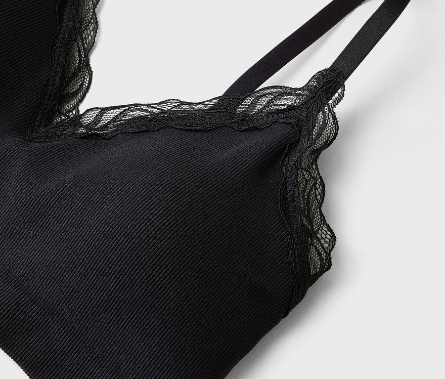 Gros plan d'un haut noir à bretelles avec des détails en dentelle sur fond blanc.