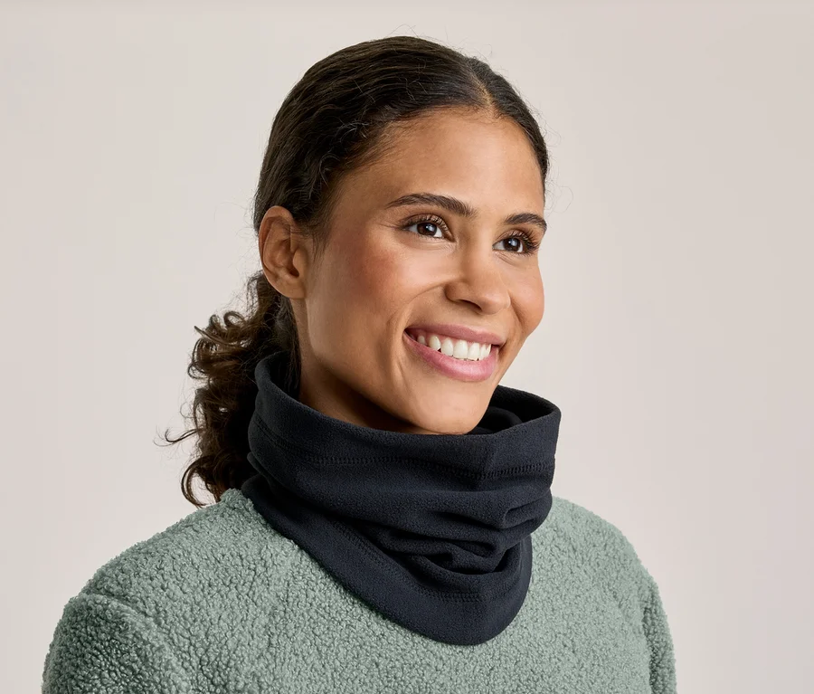 Une femme souriante aux cheveux foncés attachés porte un cache-cou noir et un haut en polaire vert menthe. Elle regarde vers la droite.