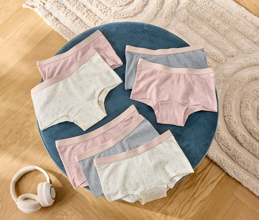 Sur un tabouret bleu sont posés six shorts pour femmes gris, roses et à pois, à côté d'un casque audio.