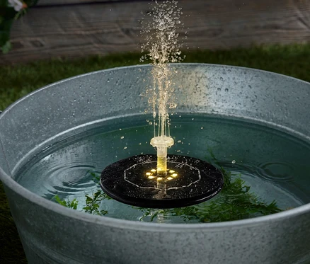 Une cuve argentée remplie d'eau dans laquelle flotte une pompe de fontaine solaire qui projette de l'eau.