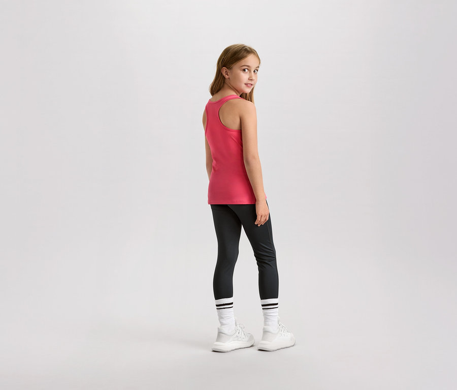 Une jeune fille regarde par-dessus son épaule, elle porte un débardeur rose, un legging et des baskets blanches.