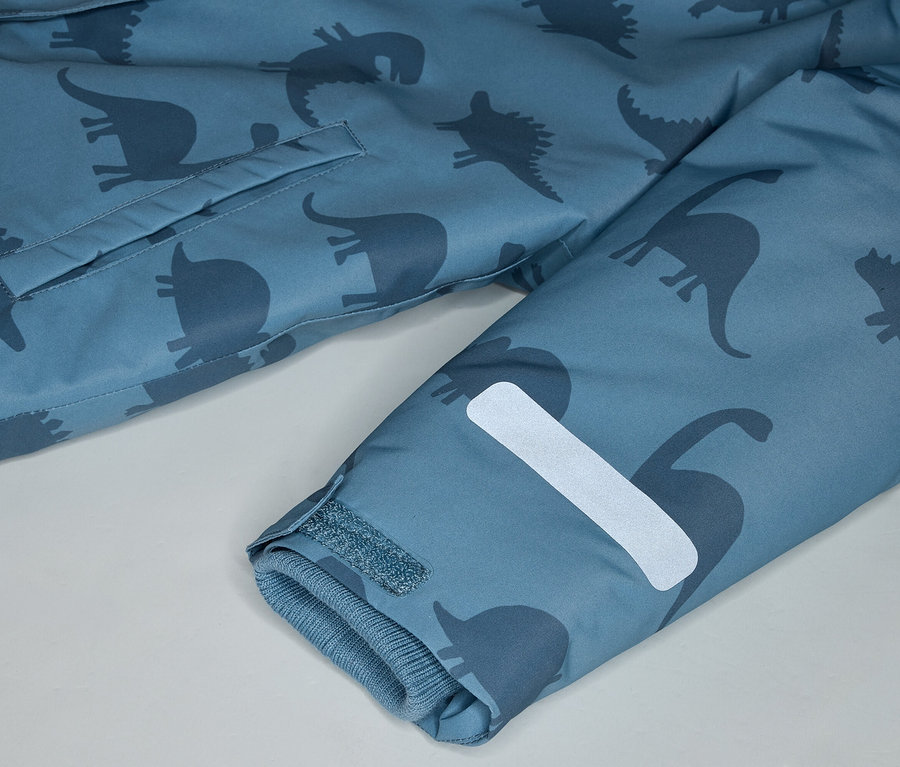 Gros plan d'un manteau bleu à motifs de dinosaures, avec une poche et une bande réfléchissante sur la manche.