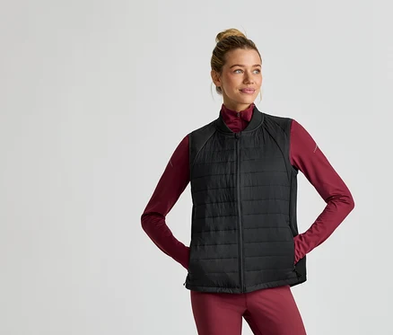 Une femme portant un chignon porte une veste noire matelassée sur un haut bordeaux à manches longues et un pantalon bordeaux.