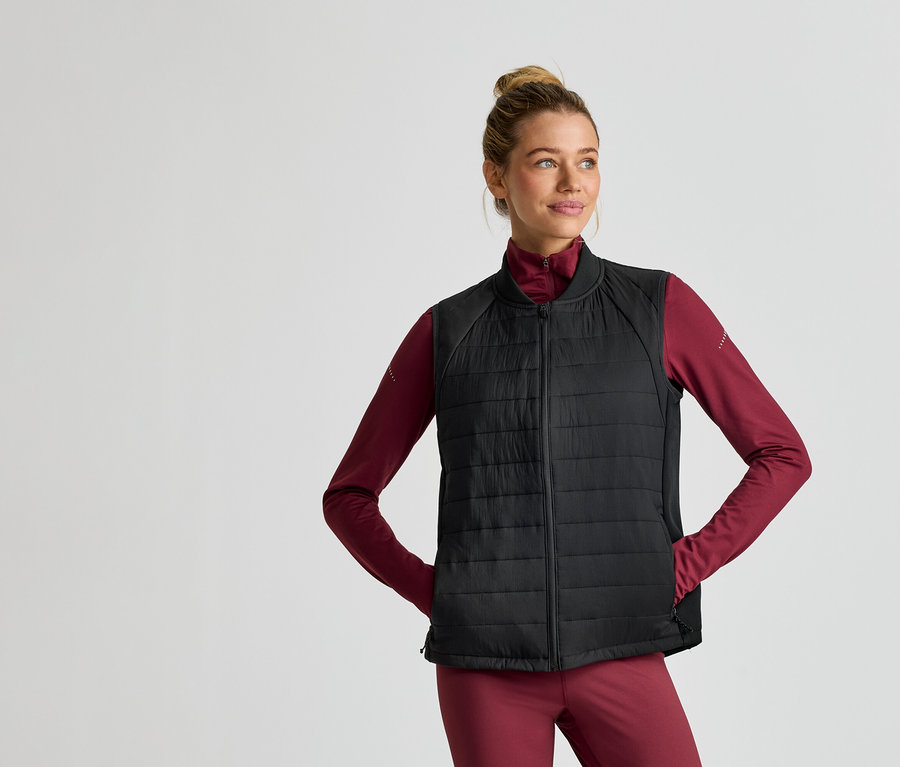 Une femme portant un chignon porte une veste noire matelassée sur un haut bordeaux à manches longues et un pantalon bordeaux.