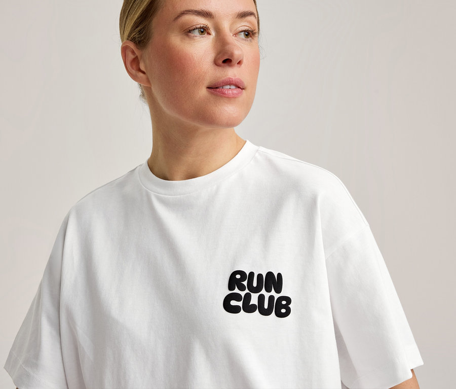Une femme porte un T-shirt de sport blanc avec l'inscription « RUN CLUB » sur la poitrine.