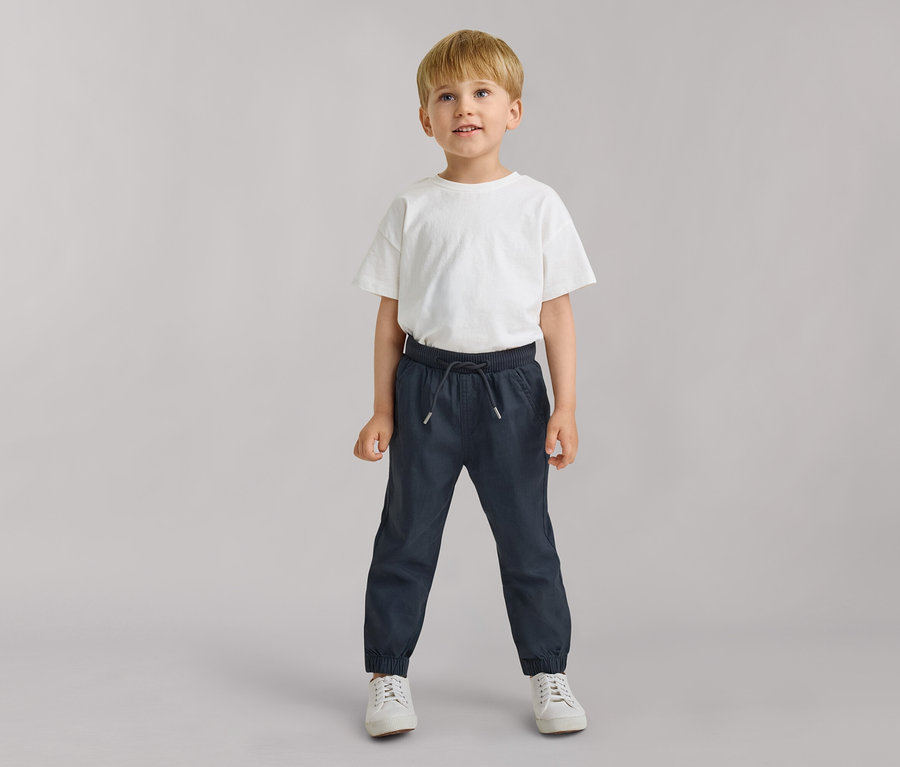 Jeune garçon portant un T-shirt blanc et un pantalon à enfiler pour enfant – Fit « Anton » bleu foncé, regardant légèrement vers le haut.