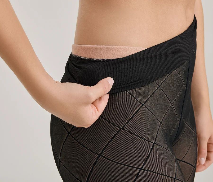 Une main tire sur la ceinture côtelée d'un collant noir à motifs, révélant un tissu beige en dessous.