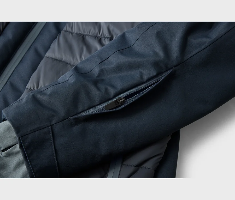 Gros plan sur une manche de veste bleu foncé avec une poche partiellement ouverte, révélant une tirette de fermeture éclair noire. Une doublure matelassée grise est visible sous la manche.
