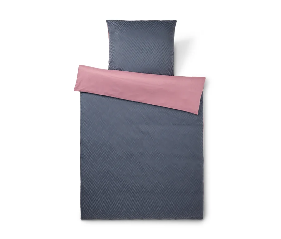 Parure de lit gris foncé avec housse de couette et taie d'oreiller à motif chevrons, avec un revers rose. La housse de couette est pliée pour montrer le côté rose.
