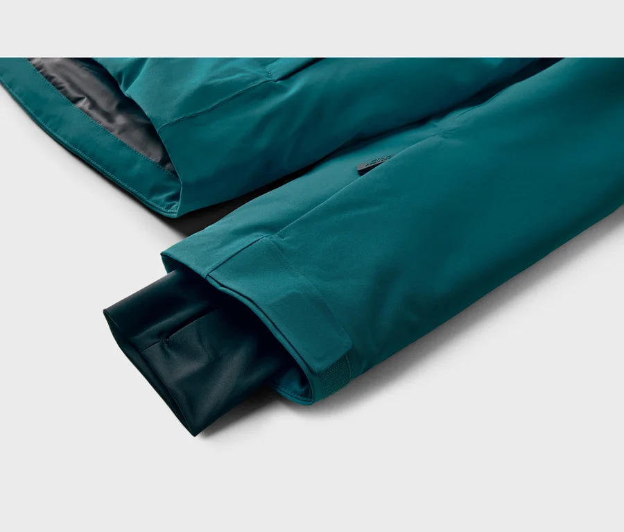 Gros plan d'une manche de veste turquoise avec un poignet intérieur, montrant une étiquette noire "ACTIVE" sur la manche extérieure.