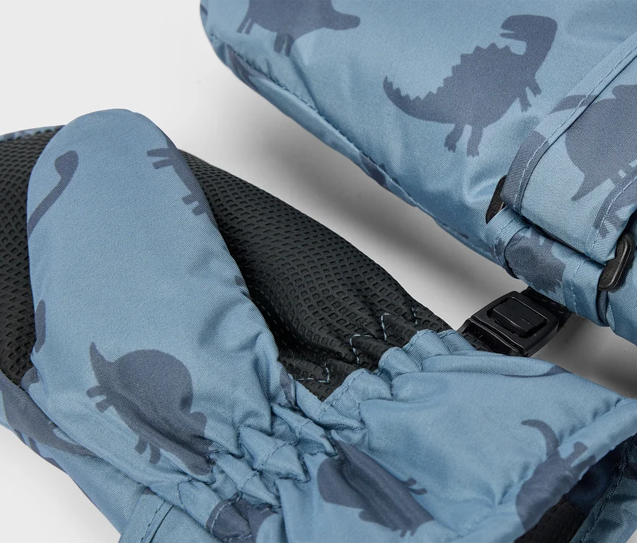 Une paire de moufles bleues avec un motif de dinosaures bleu foncé, dotées d'une paume texturée noire, d'un poignet élastique et d'une boucle noire les reliant.