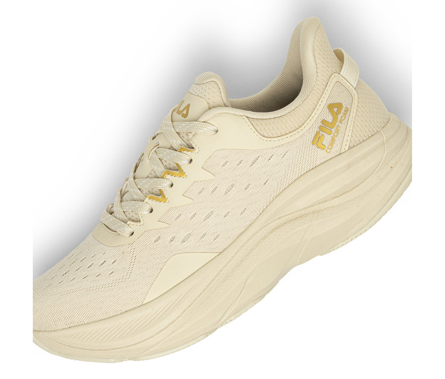 Une seule basket beige clair avec une tige en maille et une semelle épaisse et texturée. Un logo Fila doré et le texte « COMFORT FOAM » sont visibles sur le côté. Les lacets sont beiges avec des accents dorés.