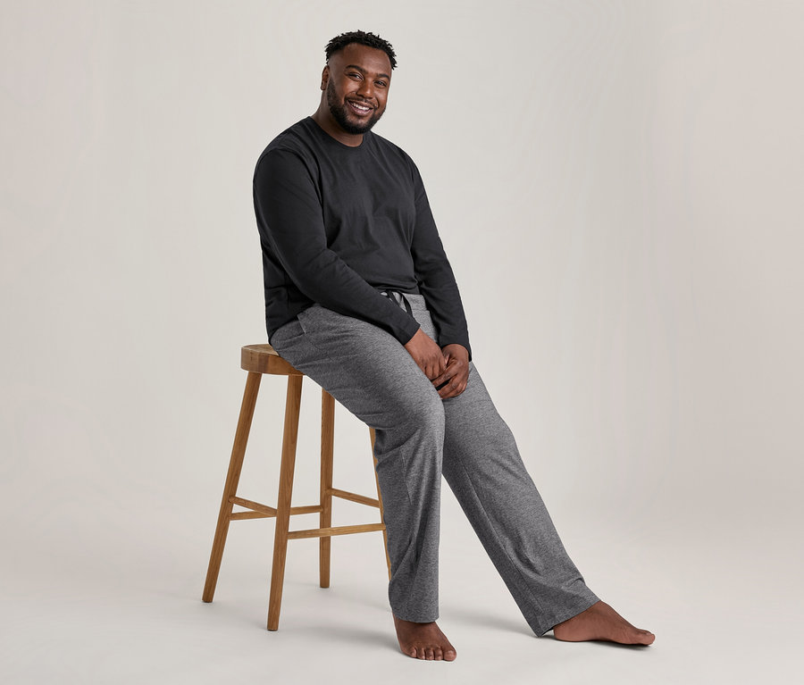 Homme souriant assis sur un tabouret, portant un ensemble pyjama noir et gris.