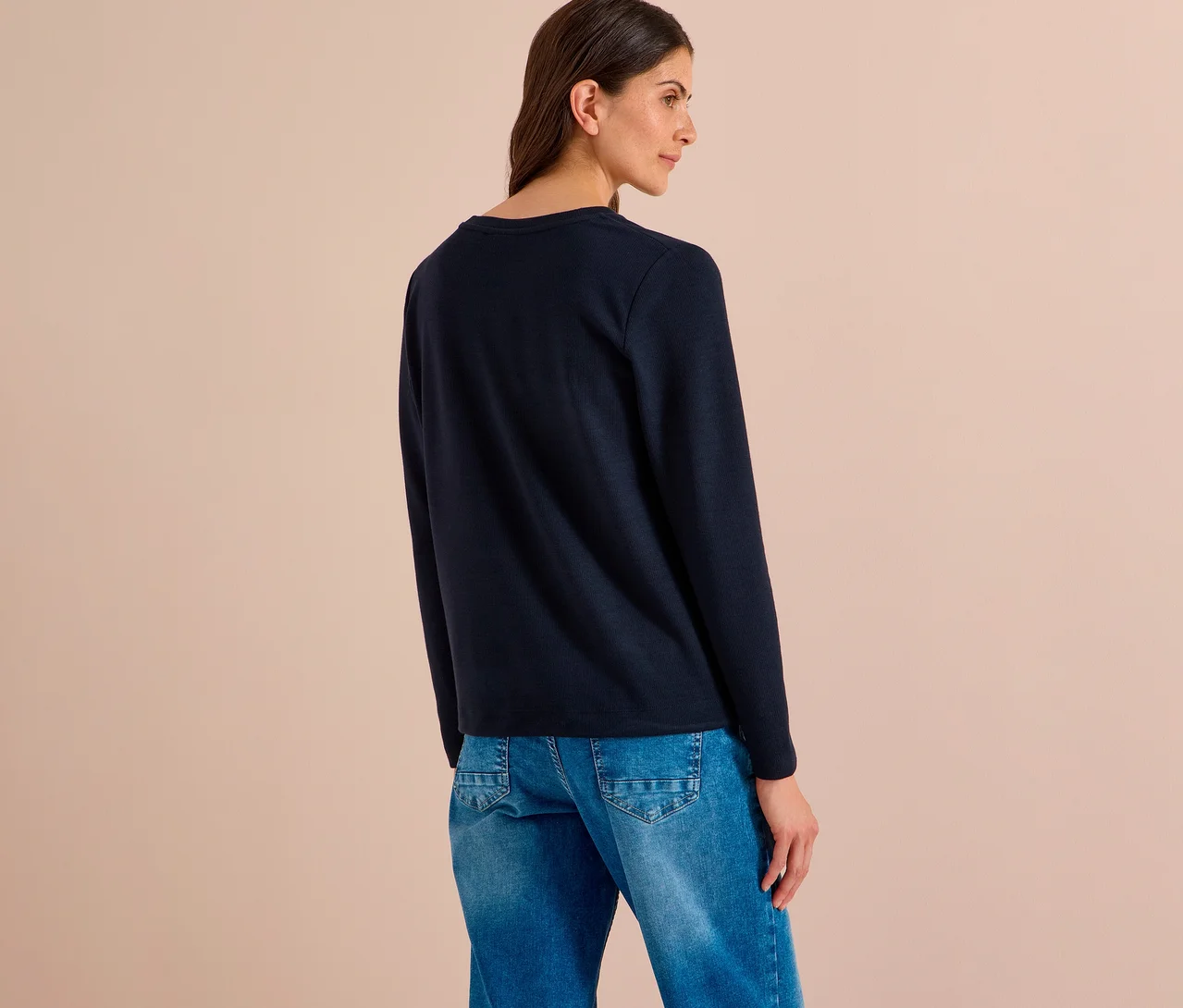 Femme vue de dos, légèrement tournée vers la droite, portant un T-shirt CECIL bleu foncé à manches longues et un jean bleu.