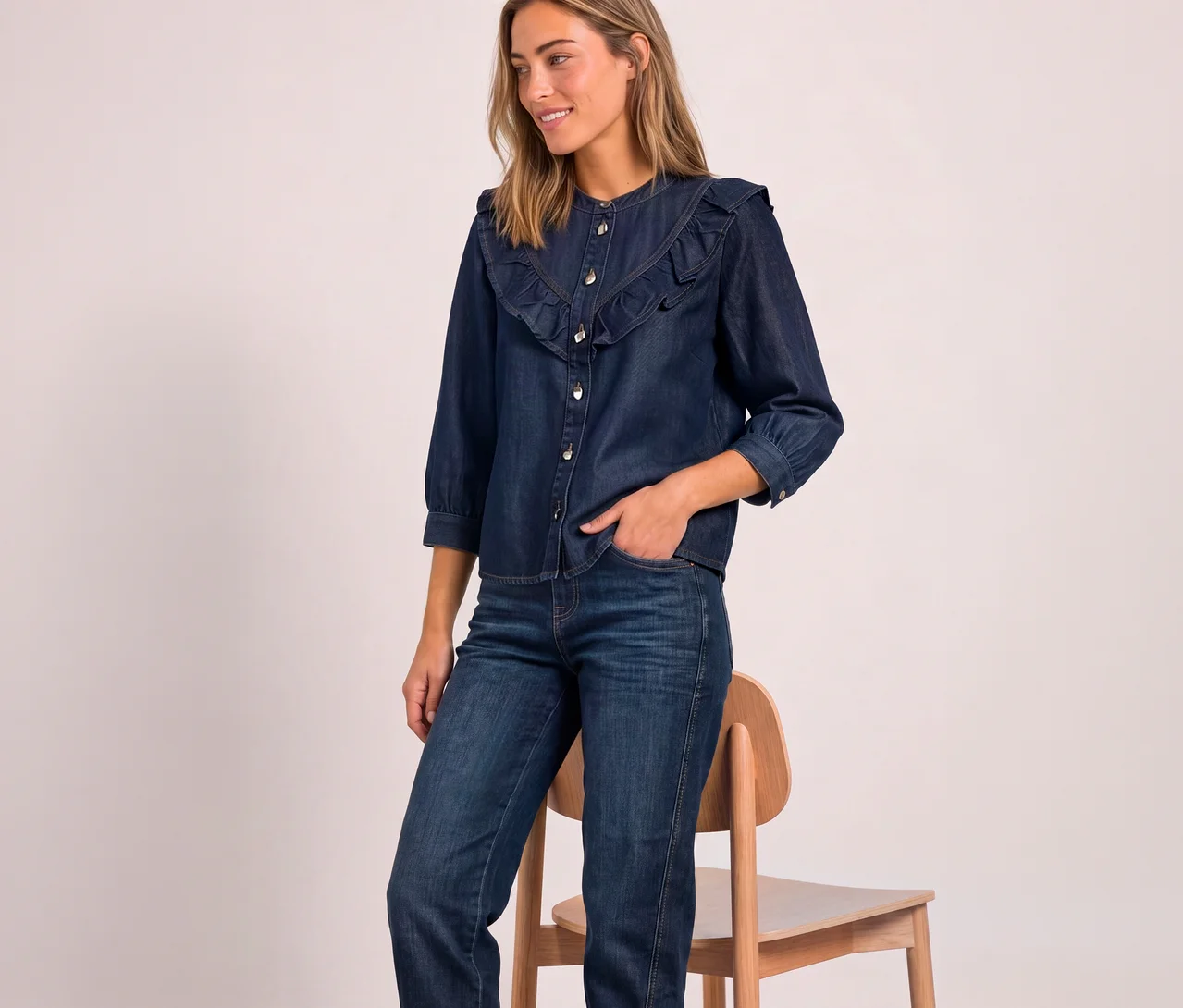 Femme souriante portant un chemisier en jean Street One bleu foncé à volants et manches trois-quarts, et un jean, une main dans la poche.