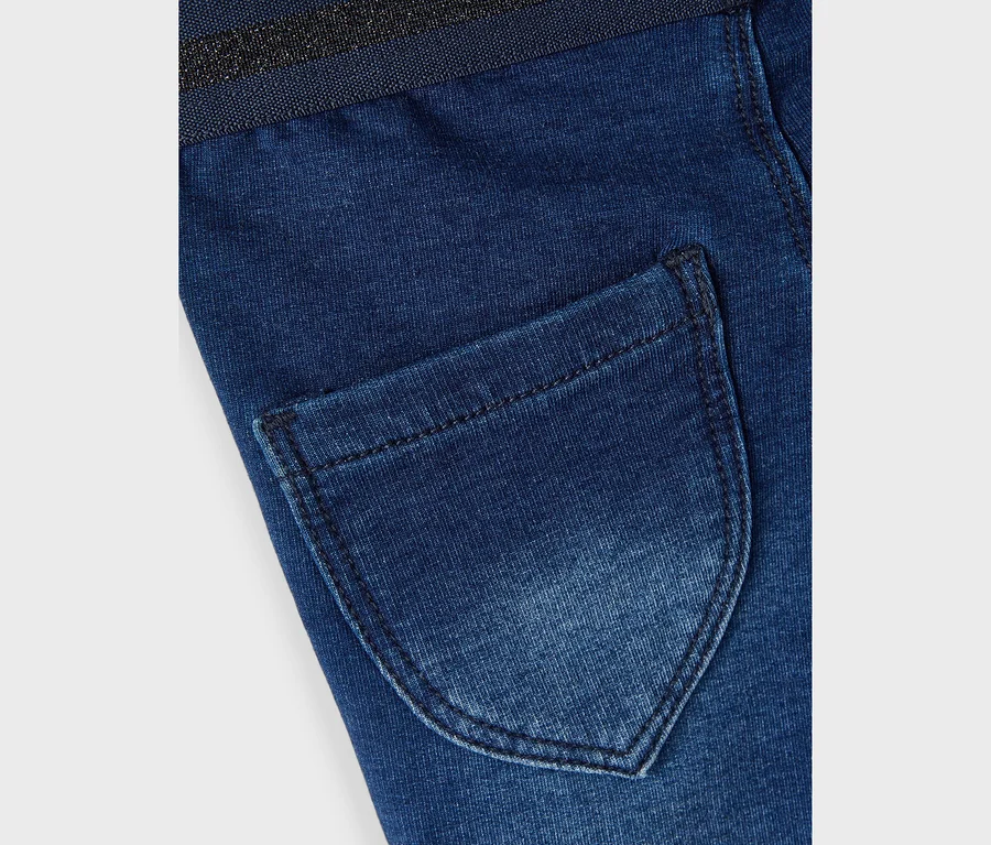 Gros plan d'un jean bleu foncé avec une poche arrière et une ceinture scintillante.