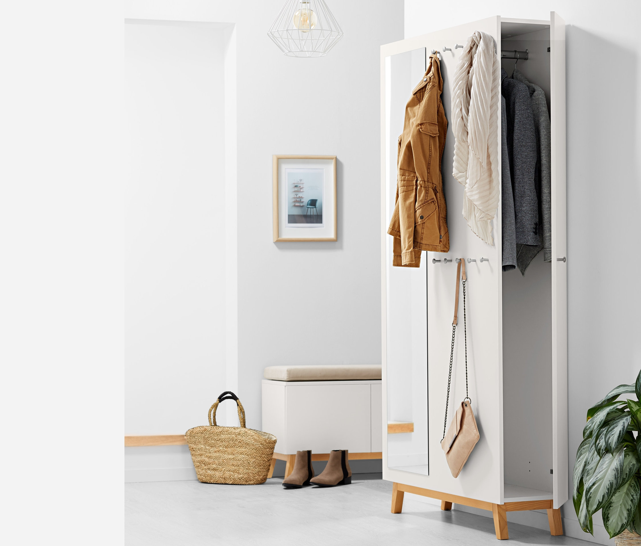 Un meuble d'entrée multifonctionnel ouvert avec une veste marron, une écharpe et un veston gris suspendus à l'intérieur, un sac à main suspendu sur le côté.