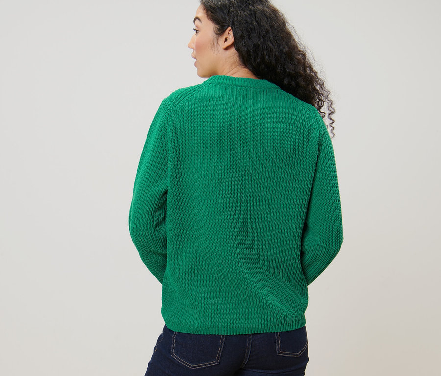 Femme regardant par-dessus son épaule portant un pull en grosse maille vert et un jean.