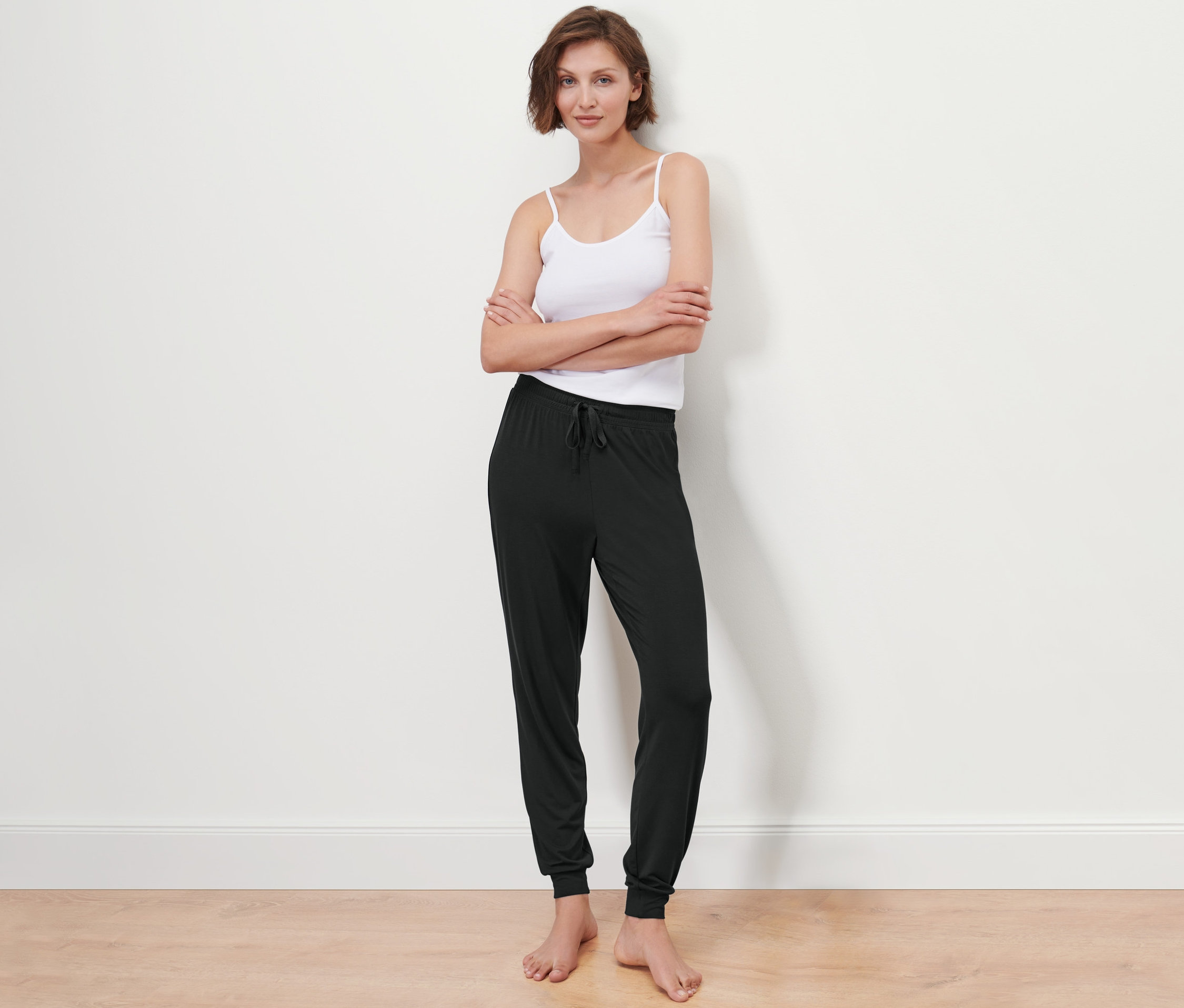 Une femme pose devant un mur blanc, vêtue d'un débardeur et d'un pantalon de pyjama.