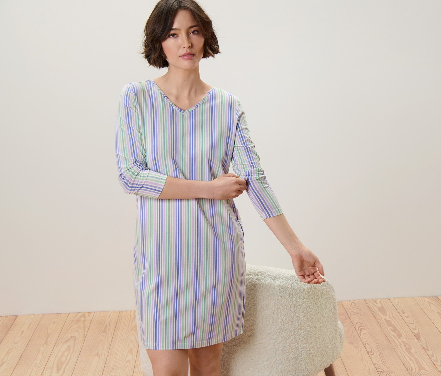 Femme remontant les manches d'une chemise de nuit rayée bleue, verte et blanche.