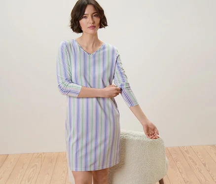 Femme remontant les manches d'une chemise de nuit rayée bleue, verte et blanche.