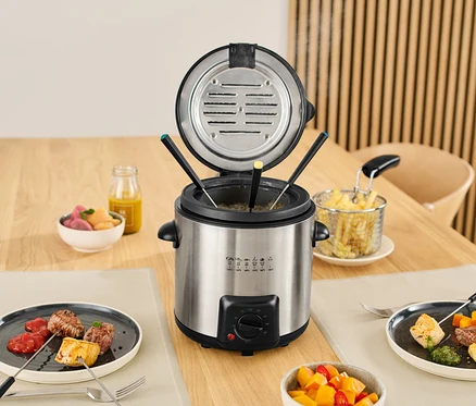 Mini friteuse et appareil à fondue sur une table avec des aliments dans des assiettes et des bols.