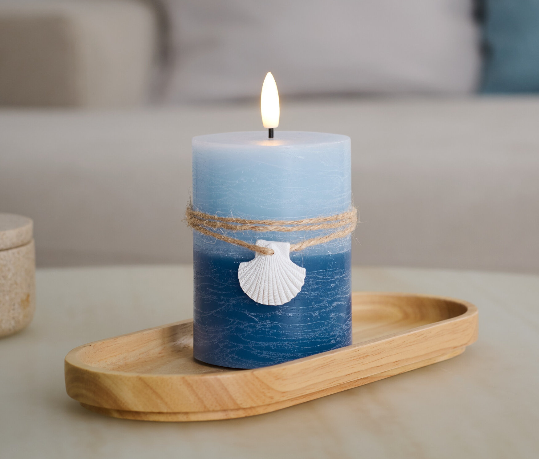 Une bougie LED bleu en cire véritable « Coquillage » sur un plateau en bois.