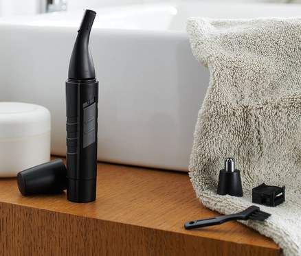 Une tondeuse nez et oreilles est posée avec ses accessoires sur une étagère en bois dans une salle de bain.