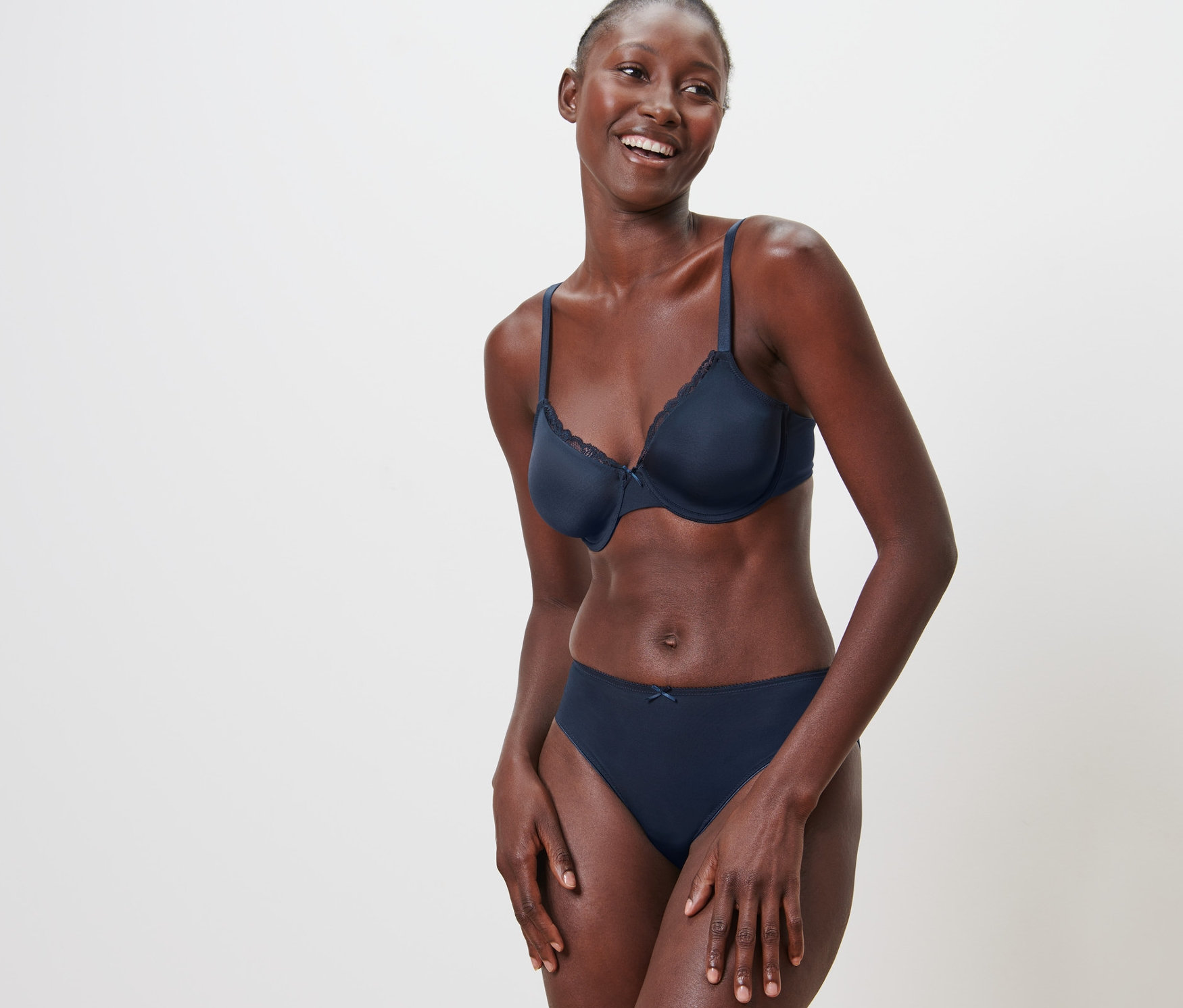 Femme souriante posant en soutien-gorge à armatures et culotte devant un fond blanc.