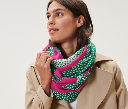 Femme portant un foulard loop imprimé vert, blanc et rose et un trench-coat beige.
