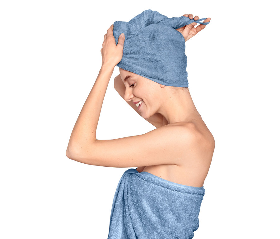 Une femme ajuste une serviette turban sur sa tête, son corps est enveloppé d'une serviette.