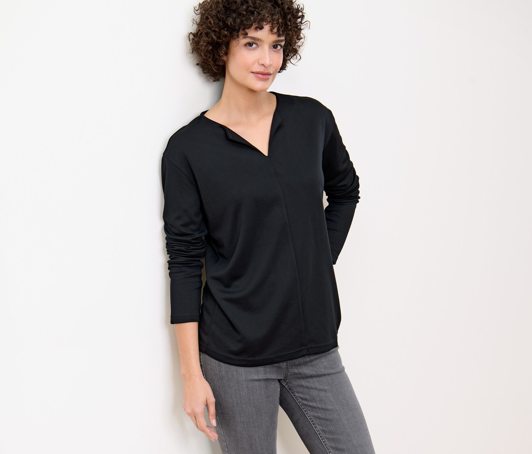 Femme appuyée contre un mur portant une blouse noire.