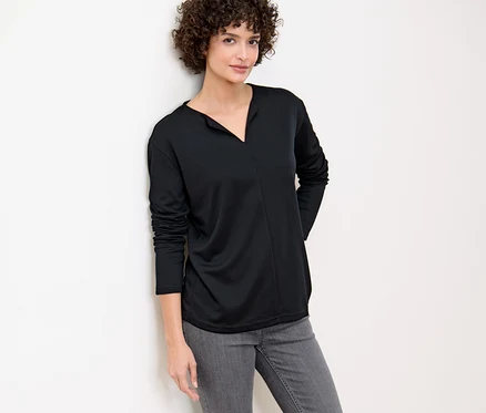 Femme appuyée contre un mur portant une blouse noire.